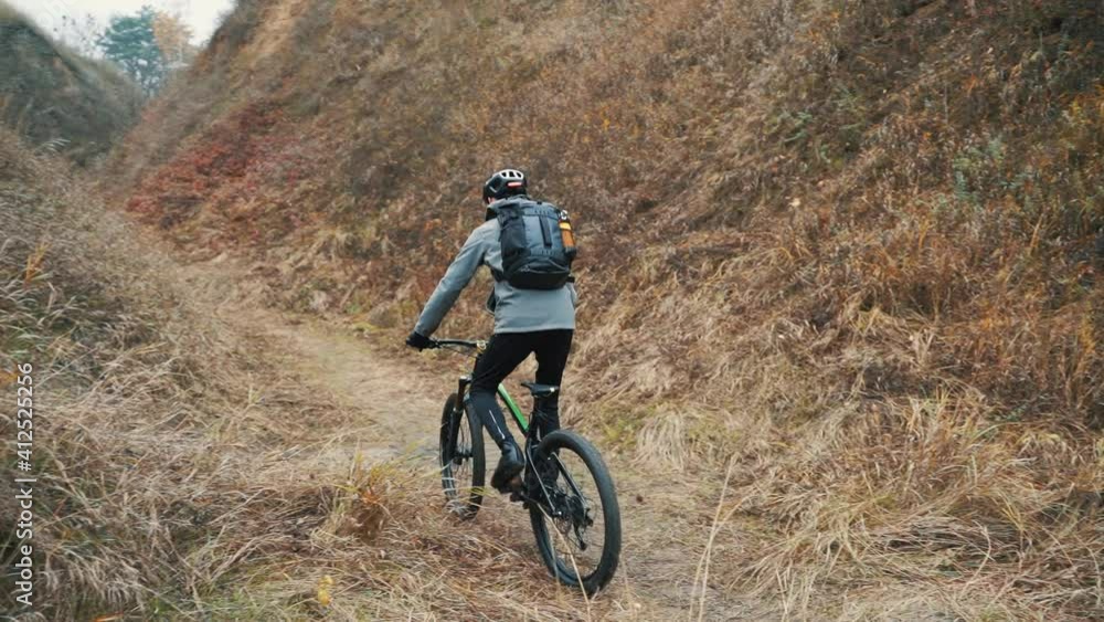Athlete male cyclist riding a mountain bike in the hill down the road in the middle of the valley Athlete male cyclist riding a mountain bike in the hill down the road in the middle of the valley