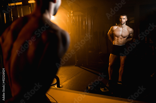 Muscular athlete posing in front of the mirror in the gym