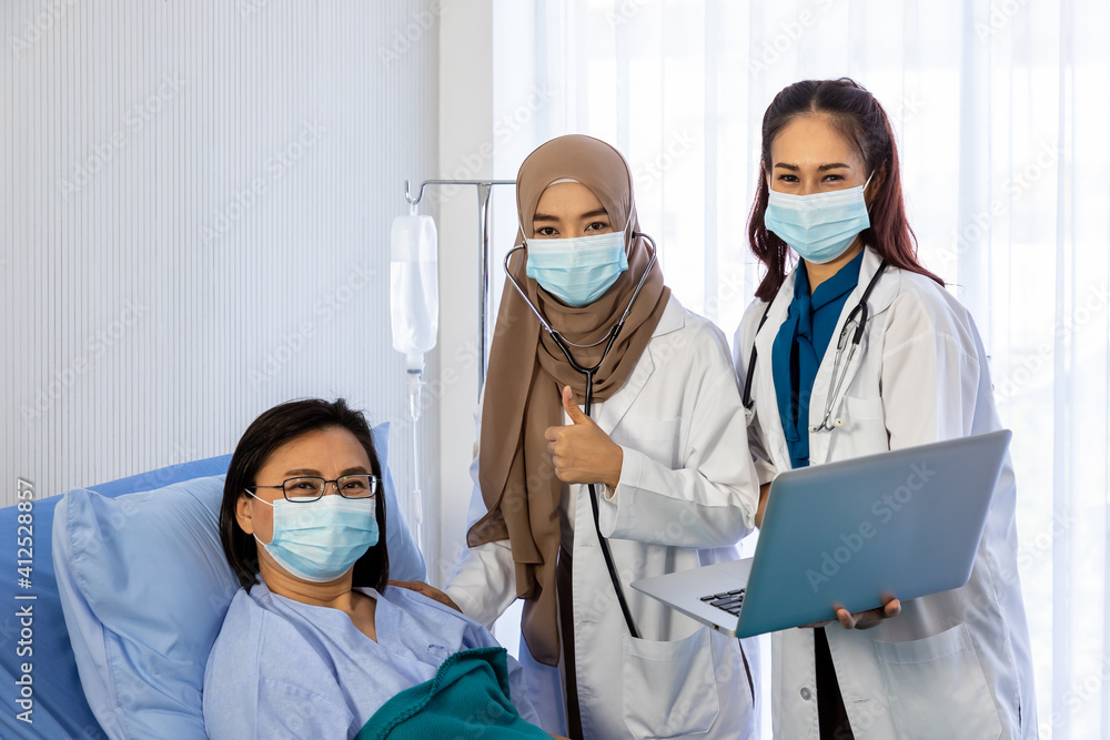 Team of doctors visiting and taking care of senior female patient in bed, with stethoscope and laptop computer, looking at camera with thumb-up. Team of doctors visiting and taking care of senior female patient in bed, with stethoscope and laptop computer, looking at camera with thumb-up.