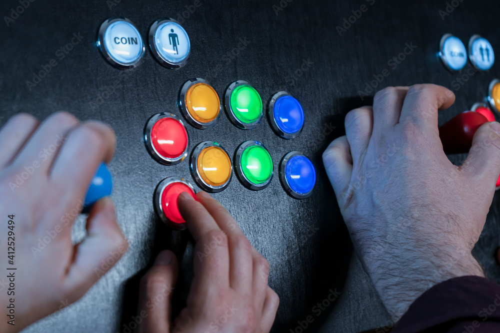 Closeup view of two people hands playing arcade vintage video games.Gamepad with joystick and many colorful buttons .Gaming concept.