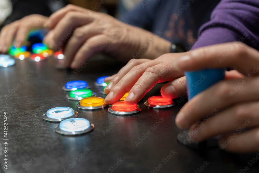 Closeup view of two people hands playing arcade vintage video games.Gamepad with joystick and many colorful buttons .Playful friends, fun and hobbies lifestyle, gaming concept. Closeup view of two people hands playing arcade vintage video games.Gamepad with joystick and many colorful buttons .Playful friends, fun and hobbies lifestyle, gaming concept.