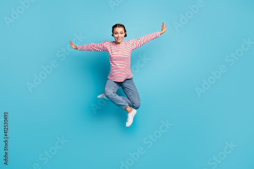 Full size photo of young attractive girl happy smile jump up hands wings fly isolated over blue color background © deagreez