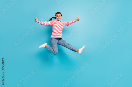 Full body photo of young excited girl happy smile jump up show thumb-up like advice cool isolated over blue color background