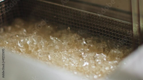 Delicious food deep frying in oil in a commercial metal fryer in a restaurant as an accompaniment to meals.