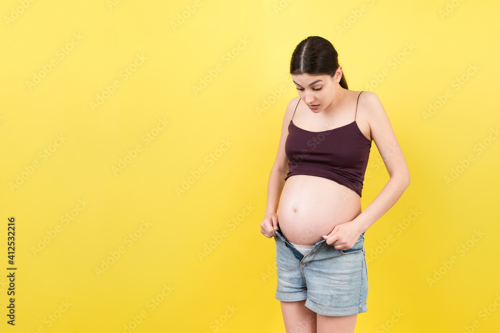 pregnant woman in unzipped jeans showing her naked belly at colorful background with copy space. Baby expecting concept pregnant woman in unzipped jeans showing her naked belly at colorful background with copy space. Baby expecting concept