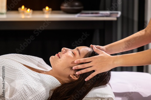 Beautiful young Asian woman enjoy head massage in tranquil spa salon, with candle.