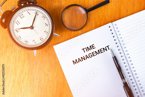 TIME MANAGEMENT concept of alarm clock, notebook and magnifying glass over wooden background with light leak in the morning.