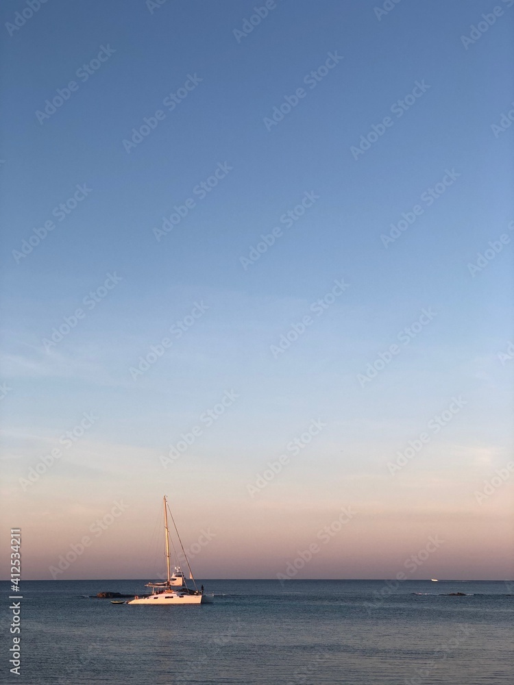 Atardecer con el cielo anaranjado y rosado en la playa cerca del mar con un barco de vela