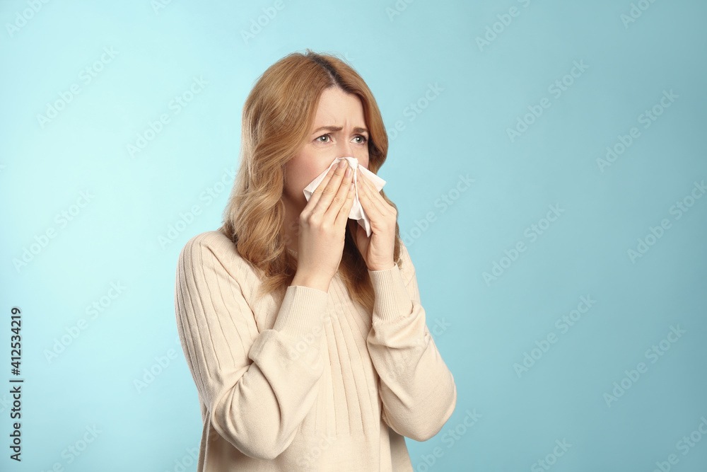Woman with tissue suffering from runny nose on light blue background. Space for text Woman with tissue suffering from runny nose on light blue background. Space for text