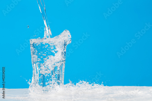 Water pouring into glass on blue background in studio