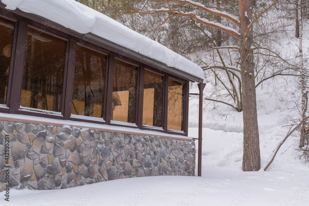 Wall of a building in a mountainous area. Solid glazing, stone wall. Background - a mountain with trees and bushes, white snow. Chalet concept. Wall of a building in a mountainous area. Solid glazing, stone wall. Background - a mountain with trees and bushes, white snow. Chalet concept.