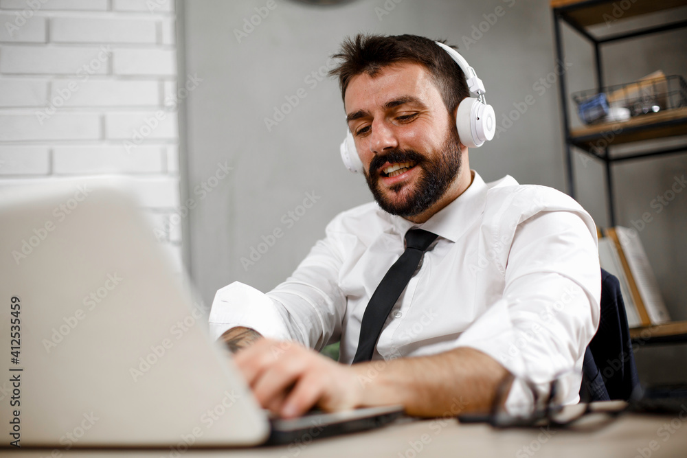 Naklejka premium Attractive businessman in office. Young businessman with headphones singing at work