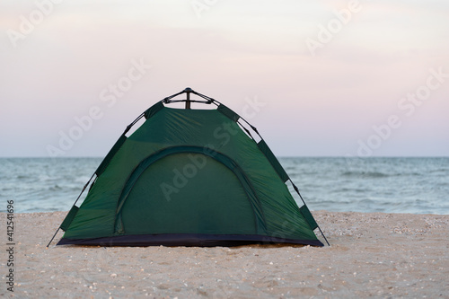 Camping. Green tent by the sea at sunset. Active tourism.