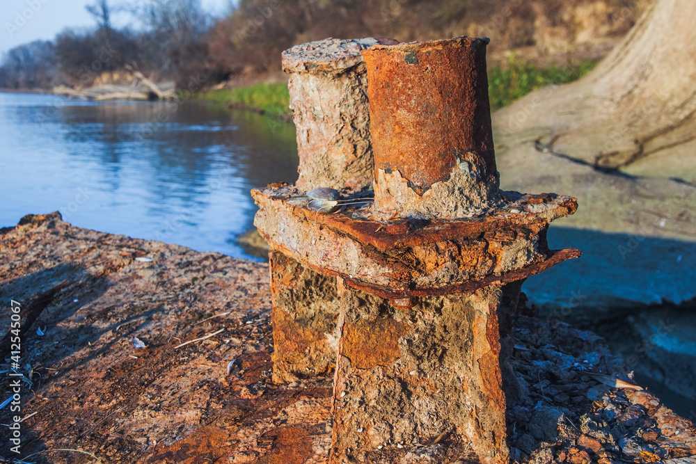 An old rusty bollard against the blue surface of the river water