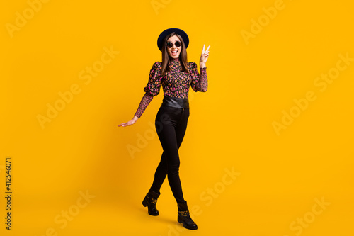 Full length body size photo of cheerful woman in stylish trendy clothes showing v-sign gesture isolated vivid yellow color background