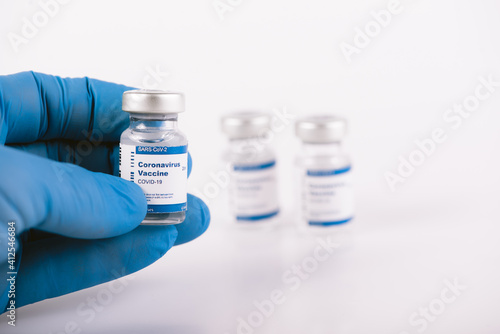 Hand with blue latex glove holding covid vaccine vial