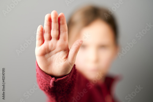Kind in einer roten Jacke streckt die Hand aus, zeigt fünf Finger und sagt Stopp