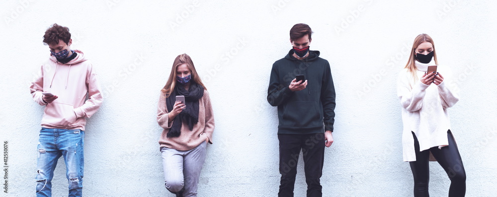 Naklejka premium Friends using mobiles covered with mask during Covid-19 out brake - Multiracial people using smart phone with face masks - New normal during pandemic - New normal lifestyle concept - Blue Filter