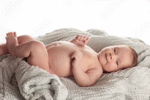 Beautiful naked baby boy lying on a knitted plaid and smiling.