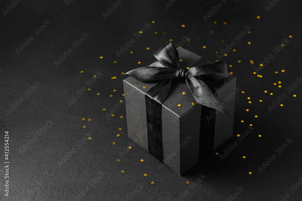 Black gift box with black bow and golden stars confetti Black gift box with black bow and golden stars confetti
