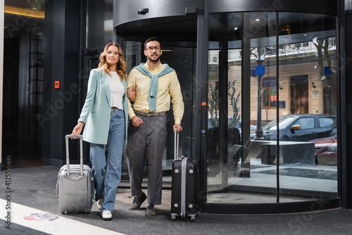 Smiling interracial couple with baggage standing near door in hotel