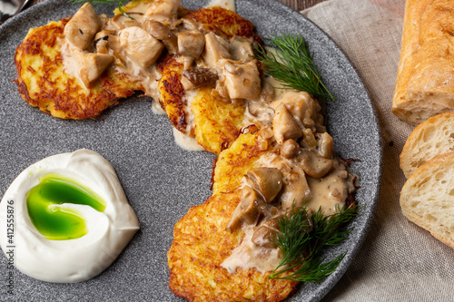 Fried potato pancakes served with mushrooms, sour cream and dill on a grey round plate with a grey linen napkin and sliced bread. Macro close-up, top view. Traditional homemade ukrainian dish. photo