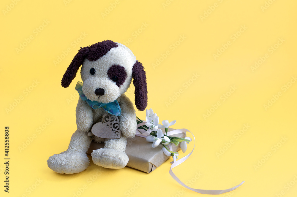 toy puppy, gift box tied with ribbon, snowdrops on a yellow background. congratulations on mother's day, March 8. toy puppy, gift box tied with ribbon, snowdrops on a yellow background. congratulations on mother's day, March 8.