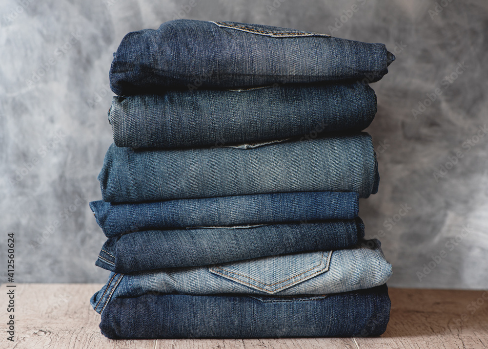 Stack of folded jeans on shelf against gray wall. Closeup of denim in different colors.