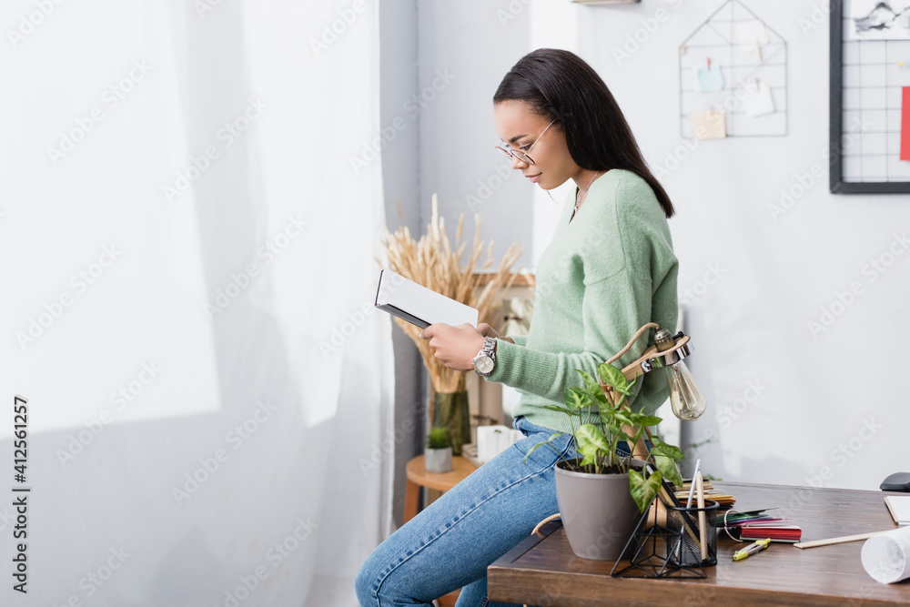 young african american architect holding notebook while sitting on work desk at home young african american architect holding notebook while sitting on work desk at home