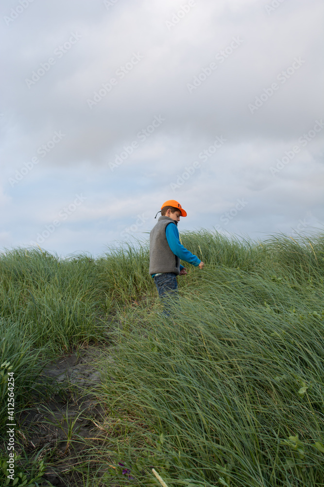 Boy climbing a sand hill covered in grasses that are blowing in the wind Boy climbing a sand hill covered in grasses that are blowing in the wind