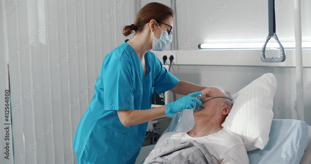 Nurse putting oxygen mask on senior male patient lying in hospital bed Nurse putting oxygen mask on senior male patient lying in hospital bed