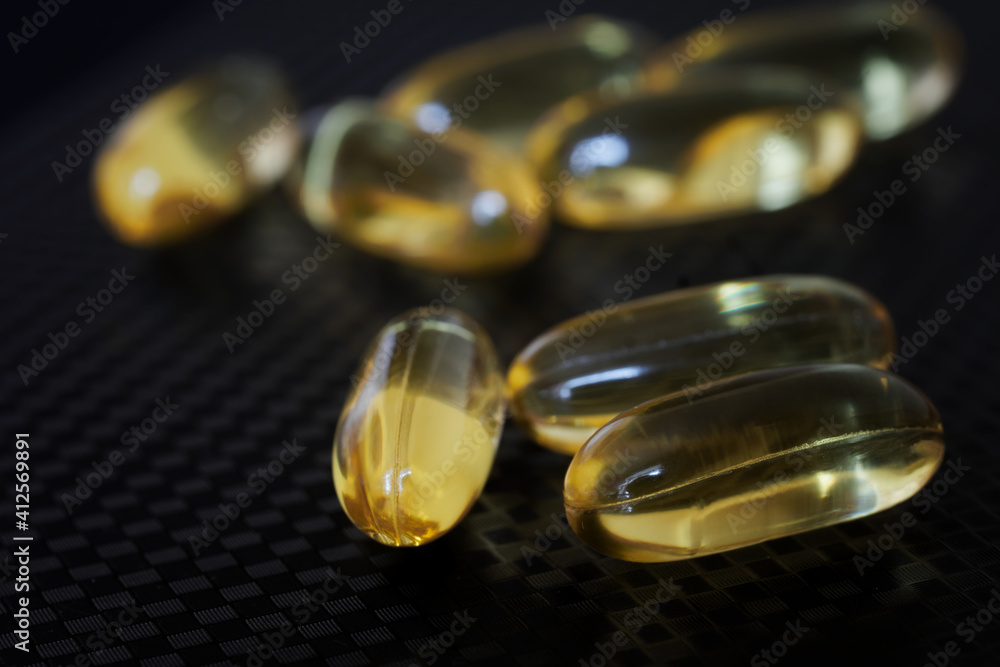 Transparent capsules with fish oil lie on a black textured surface. Medicines and prevention of viral diseases. Selective focus. Macro Transparent capsules with fish oil lie on a black textured surface. Medicines and prevention of viral diseases. Selective focus. Macro