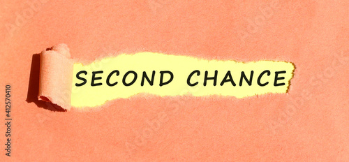 The text SECOND CHANCE appearing on yellow paper behind torn color paper. Top view.
