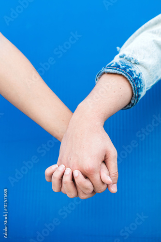 Close up of the holding hands of a young couple in love with blue wall