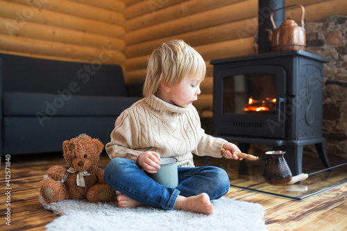 Cute toddler child in a little fancy wooden cottage, reading a book, drinking tea photo