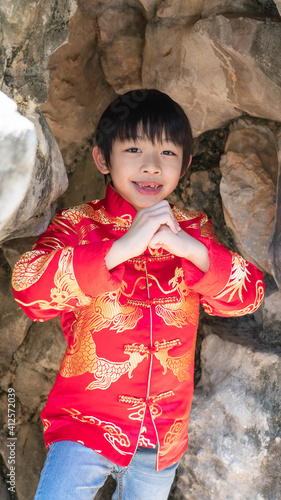 An Asian happy kid with a lovely smiling expression.A Chinese boy in tradition clothes during Lunar New Year with two hands up to respect or bless someone. photo