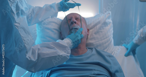 Medical stuff adjusting oxygen mask on senior man lying in hospital bed fighting with coronavirus