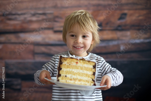 Cute toddler blond child, holding cake and looking