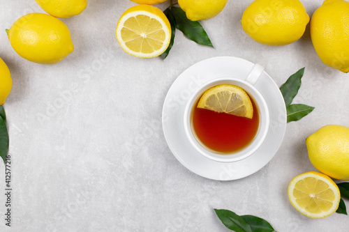 Cup of tea with fresh lemons and leaves on white concrete stone background. Hot healthy beverage. Immune defence, vitamin c. Top view. Copy space.