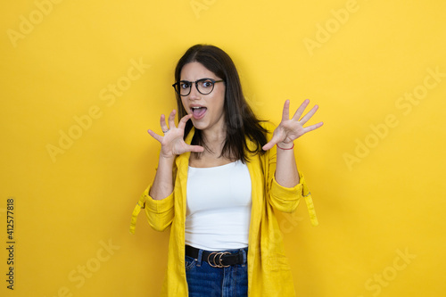 Young brunette businesswoman wearing yellow blazer over yellow background smiling funny doing claw gesture as cat, aggressive and sexy expression © Irene