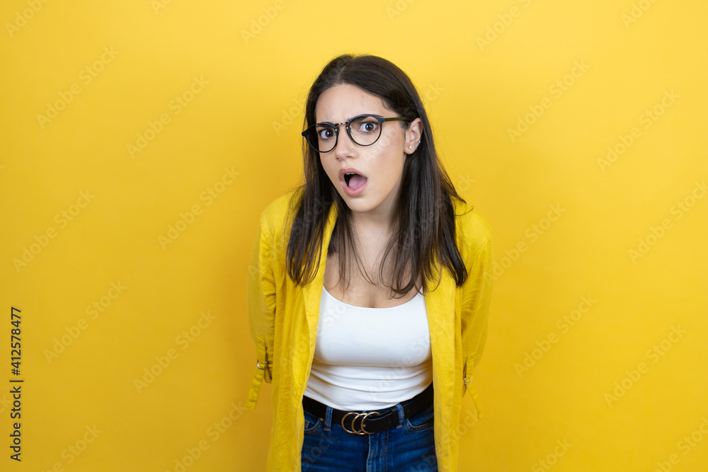Young brunette businesswoman wearing yellow blazer over yellow background afraid and shocked with surprise and amazed expression, fear and excited face. Young brunette businesswoman wearing yellow blazer over yellow background afraid and shocked with surprise and amazed expression, fear and excited face.