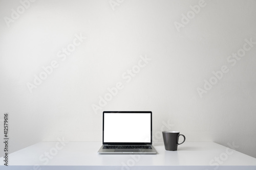 Modern contemporary workspace with blank screen laptop computer and coffee cup on office desk table on white background for copy space. Home office workplace concept.