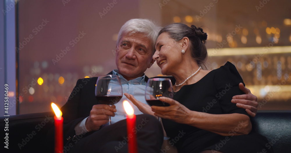 Senior husband and wife drinking red wine relaxing on couch in restaurant