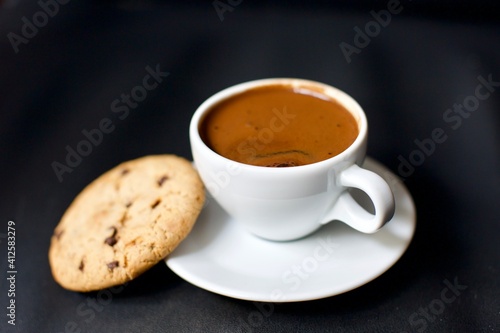 Turkish coffee in a white porcelain glass and chocolate chip cookies. Blurry and black background.