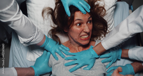 Fototapeta Top view of doctors in latex gloves holding mad screaming woman trying to escape