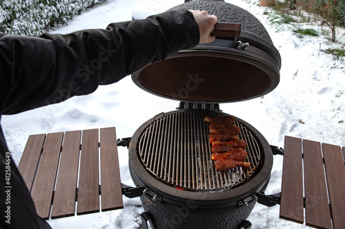 Winter bbq in the fresh white snow, Men grilling chicken wings in the winter onn grill photo