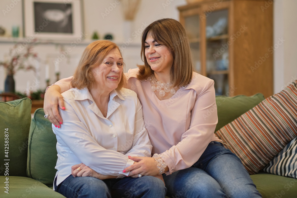 middle aged female visiting her mother, sitting together on comfortable couch, having good conversation. Woman in her forties talking to daughter at home