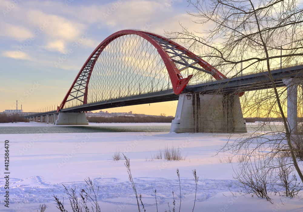 Obraz premium Winter morning on the Ob. The arch of the Bugrinsky automobile bridge on the frozen river bank in Novosibirsk