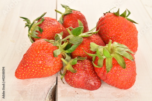 A group of several bright red strawberries, close-up, on a painted wooden table.