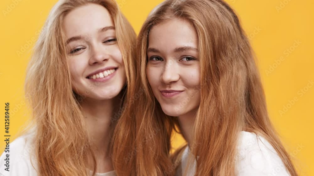 Youth and happiness. Close up portrait of two cheerful redhead twin sisters laughing to camera, orange background Youth and happiness. Close up portrait of two cheerful redhead twin sisters laughing to camera, orange background